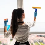 Primer plano de una mano limpiando cuidadosamente el perfil blanco de una ventana de PVC en Madrid con agua y jabón neutro.