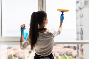 Primer plano de una mano limpiando cuidadosamente el perfil blanco de una ventana de PVC en Madrid con agua y jabón neutro.
