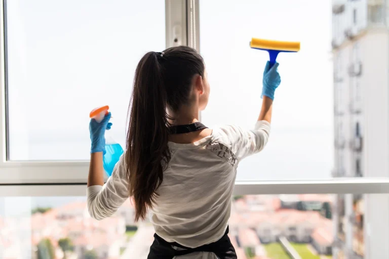 Primer plano de una mano limpiando cuidadosamente el perfil blanco de una ventana de PVC en Madrid con agua y jabón neutro.